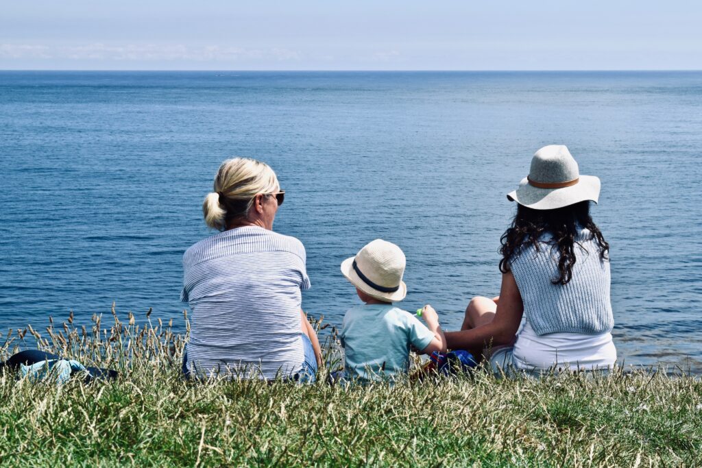 mother and grandmother sitting with toddler by the ocean