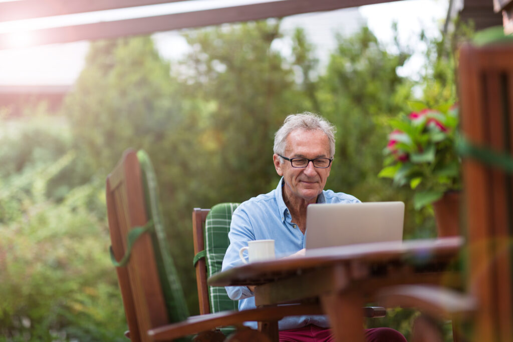 senior man working on his laptop outside on his patio
