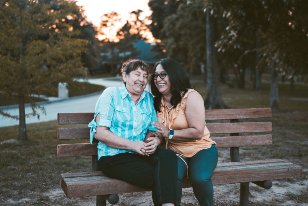 woman sitting with her older mother on a park bench laughing together