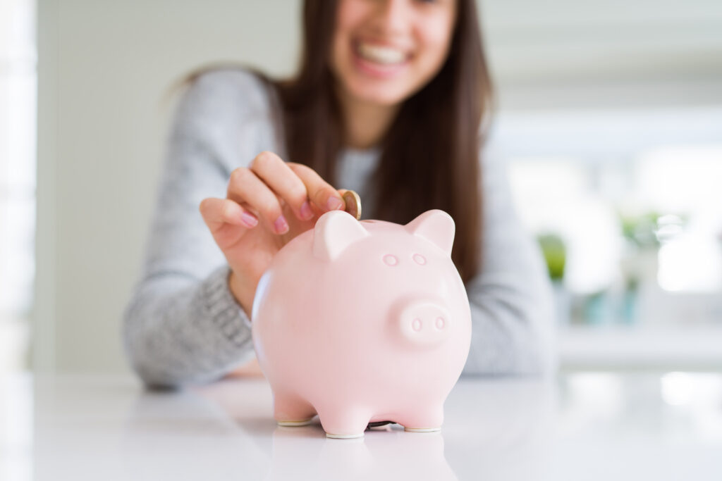 young woman smiling happily and placing a quarter into a piggy bank