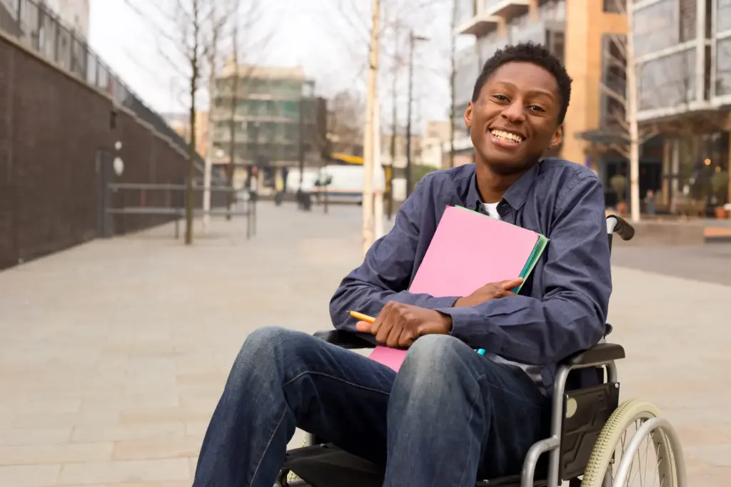 young man in a wheelchair smiling and holding folders