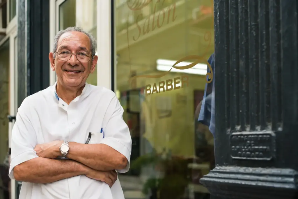 older barbershop owner smiling in front of his shop